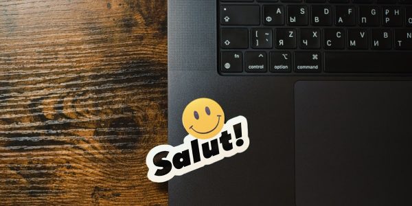 Laptop with a "salut!" smiley sticker on keyboard.
