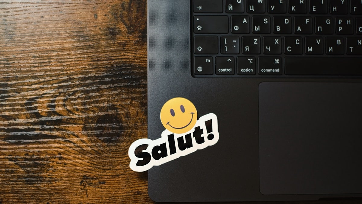 Laptop with a "salut!" smiley sticker on keyboard.