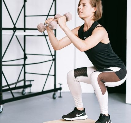 A woman in sportswear performs a squat with dumbbells indoors, embodying strength and healthy living.